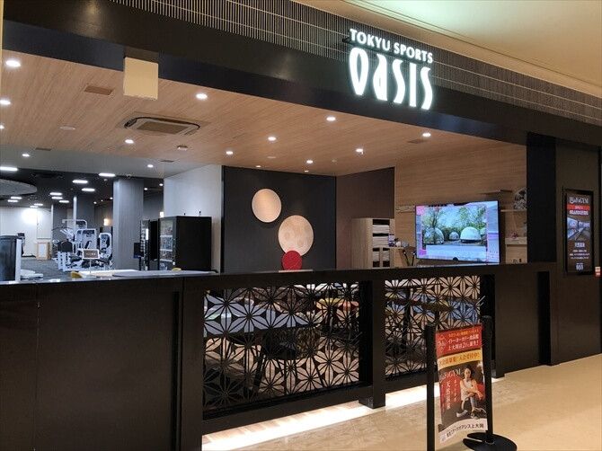 東急スポーツオアシス上大岡::和モダンなエントランス。フェンスの格子模様も和柄で、モチーフとなっているのは立地する港南区のシンボルのひとつとなっている桔梗（キキョウ）。フェンスの向こうはワークショップなどの開催も予定されている交流スペースのラウンジエリアです。